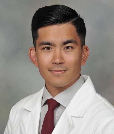 Dr. Joshua Tsau in a white coat, grey shirt and maroon tie.
